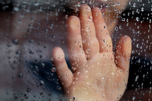 Kinderhand an einer Glasscheibe voller Regentropfen