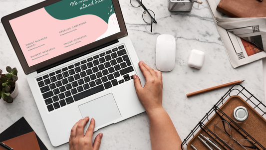 Titelbild zeigt eine Frau am Laptop mit Smartphone, Maus, Papieren und typischen Arbeitsmaterialien – Sinnbild für digitales Arbeiten und Business.