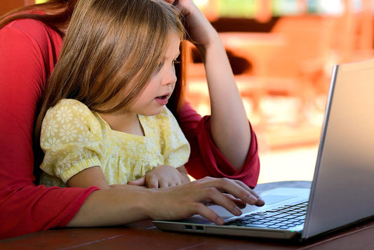 Ein Kind sitzt auf dem Schoß seiner Mutter und schaut auf einen Laptop. Von der Mutter ist nur der Oberkörper ohne Kopf zu sehen – Symbol für die Vereinbarkeit von Familie und Beruf.